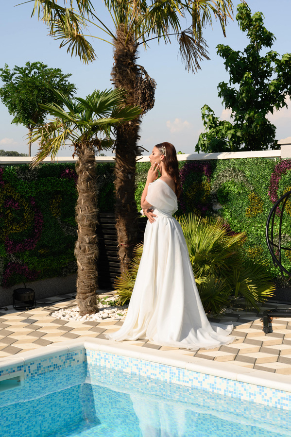 Mlada stoji pored bazena tokom venčanja na otvorenom u Beogradu – elegantna i svetlosno nežna scena u umetničkom stilu, snimljena od strane MI Weddings.